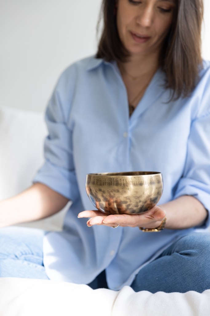 Een vrouw in een blauwe blouse houdt een gouden kom vast terwijl ze op een witte bank zit.