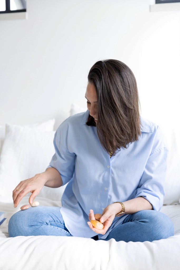Een vrouw zit op een bank en houdt verschillende kristallen in haar handen, terwijl ze naar beneden kijkt.