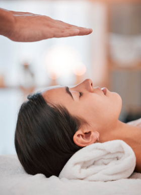 Een hand die boven het hoofd van een ontspannen vrouw hangt tijdens een Reiki-sessie.